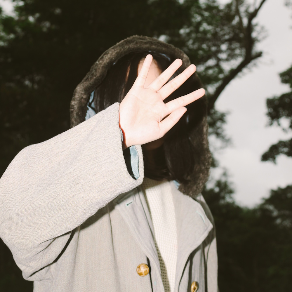Woman outdoors placing her hand to her face to block a photograph from being taken